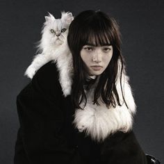 a woman holding a white cat on her shoulders in front of a blue background,