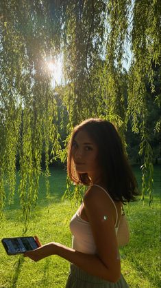 a woman standing under a tree holding an electronic device