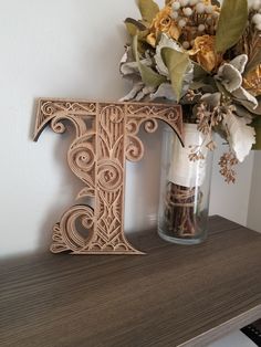 a wooden letter sitting on top of a shelf next to a vase filled with flowers