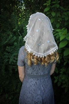 a woman wearing a veil over her head in front of some trees and bushes,