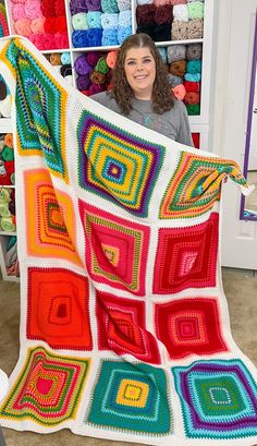 a woman holding up a colorful crocheted blanket