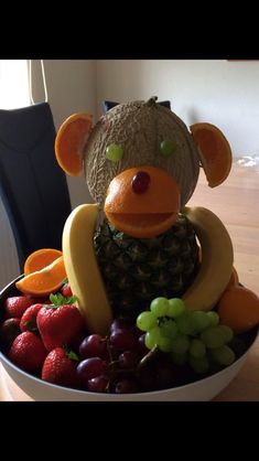 a bowl filled with fruit and an animal made out of grapes, oranges, strawberries