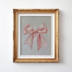 a gold frame with a pink bow hanging on the wall next to a white wall