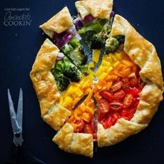 a colorful vegetable pie is cut into four sections and sits on a blue surface next to a pair of scissors