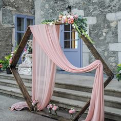 an outdoor ceremony setup with pink draping and flowers on the steps, next to a blue door