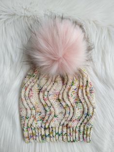 a knitted hat with a pink pom - pom sitting on top of it