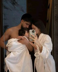 a man and woman wrapped in white towels taking a selfie with their cell phone