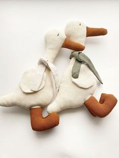 two stuffed ducks sitting next to each other on a white surface, one with an orange beak