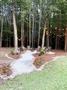 an outdoor seating area surrounded by trees with lights strung from the top and flowers on the ground