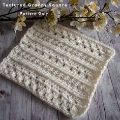 a white crocheted square sitting on top of a wooden table next to flowers