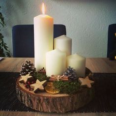 three white candles sitting on top of a wooden table next to pine cones and other decorations