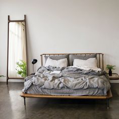 an unmade bed sitting in a bedroom next to a mirror and potted plant