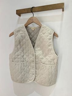 a white quilted vest hanging on a wooden hanger