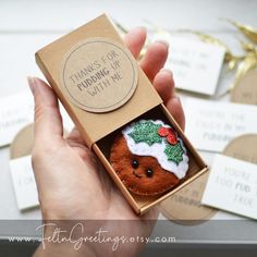 a hand holding a small christmas ornament in a box with tags around it