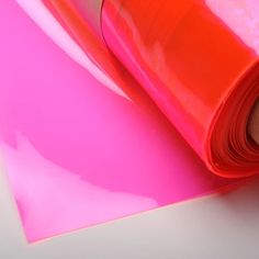 a roll of pink colored paper sitting on top of a white table next to an orange piece of plastic