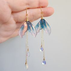 Discover the beauty of iridescent mermaid tail earrings in this stunning collection. These unique and eye-catching accessories are sure to make a splash wherever you go. Perfect for adding a touch of whimsy and magic to any outfit. Whether you're attending a wedding, a formal event, or simply want to add a touch of fierceness to your everyday look, these earrings are a versatile and stylish choice. 🍊Material: The earrings are made with shimmering resin mermaid tails, Czech glass water drops and the 14K gold plated (nickel-free) hooks. Handmade in Maryland, USA! 🌺Size: approx.(W x L) 2.54cm x 9.5cm 🎀Handmade jewelry: Each item is made to order, which gives our pieces a unique meaning that is specific and special to you.Therefore, there are no two items exactly alike. Contains small parts Magical Jewelry Fantasy Earrings, Mermaid Tail Jewelry, Diy Mermaid Accessories, Iridescent Fantasy Jewelry For Parties, Fantasy Iridescent Jewelry For Parties, Mermaid Jewelry Aesthetic, Mermaid Tail Aesthetic, Mermaid Jewellery, Mermaid Tail Earrings