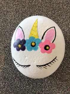 a painted rock with an unicorn's face and flowers on it