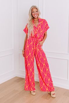 - Stroll into style with this trendy jumpsuit, where laid-back vibes meet botanical beauty. Its relaxed silhouette, adorned with a charming abstract leaf print, is complemented by a collared neckline and a drawstring cinched waistline, ensuring both comfort and flair. Effortlessly chic, it's your go-to for relaxed outings or leisurely escapes, promising a blend of ease and sophistication that's as laid-back as it is refined. - Unlined material with an abstract leaf print featuring pink and orang Casual V-neck Jumpsuits And Rompers With Tropical Print, Chic Summer Jumpsuits And Rompers With Vibrant Print, Spring Day Out Tropical Print Jumpsuit, Spring Tropical Print Jumpsuits And Rompers For Day Out, Spring Tropical Print Jumpsuit For Day Out, Spring Beach Collared Jumpsuits And Rompers, Spring Beach Jumpsuits And Rompers With Collar, Collared Jumpsuits And Rompers For Beach In Spring, Collared Jumpsuits And Rompers For Spring Beach