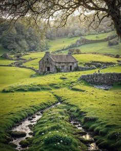 an old stone house sitting on top of a lush green field next to a stream