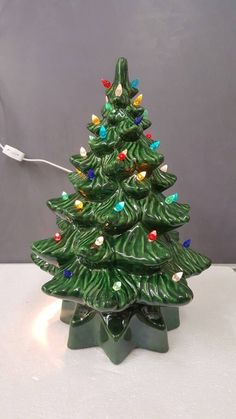 a small green ceramic christmas tree with lights on it's base and an electric cord plugged into the top