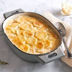 a casserole dish is shown on a table with silver spoons and flowers