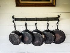 four pots and pans hanging on a wall with a painting in the back ground