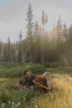 a man and woman sitting in the grass with their dog, both holding each other