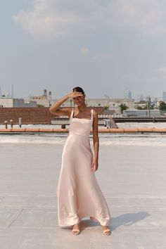 a woman in a pink dress is standing on the roof with her hands behind her head