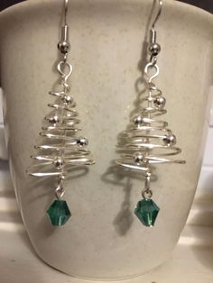 a pair of silver wire earrings with green crystal beads on top of a white cup