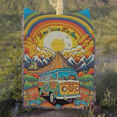 an old vw bus tapestry hanging on the side of a road with mountains in the background