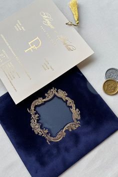 a blue and gold wedding card with a golden frame on it next to two coins