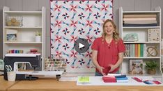 a woman standing in front of a table with quilts on it and a wall hanging behind her