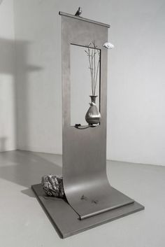 a metal sculpture with vases and rocks in the middle on a white floor next to a wall