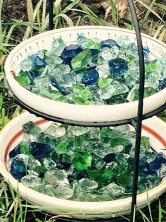 two white bowls filled with green and blue glass chips sitting on top of a grass covered field