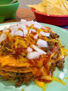 a green plate topped with lasagna covered in cheese and onions next to chips