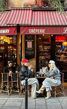 two people sitting at a table in front of a store with red awnings