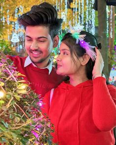 a man and woman standing next to each other in front of a christmas tree with lights