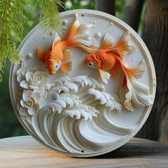 two gold fish are in the center of a white plate with flowers and waves on it