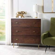 a green chair sitting in front of a dresser with a gold elephant statue on top