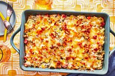 a casserole dish with meat, cheese and vegetables on a yellow patterned tablecloth