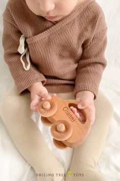 a baby sitting on top of a bed holding a wooden toy