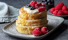 a stack of pancakes topped with berries and whipped cream on a plate next to some raspberries