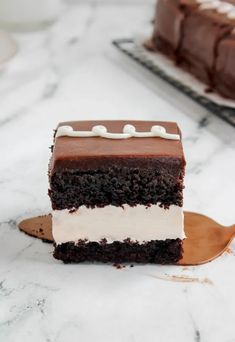 a piece of chocolate cake with white frosting on a wooden spoon next to a slice of cake