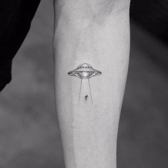 a small tattoo on the leg of a person with an alien ship flying above it