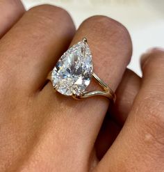 a woman's hand holding a ring with a pear shaped diamond