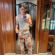 a woman taking a selfie in front of a door wearing floral pants and tank top