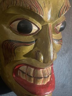 a wooden mask with large eyes and mouth painted yellow, red and black on the face