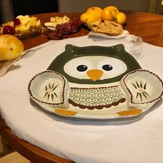 an owl shaped plate sitting on top of a table next to oranges and grapes