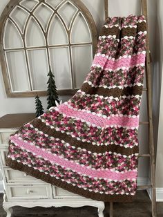 a pink and brown blanket sitting on top of a white dresser next to a window