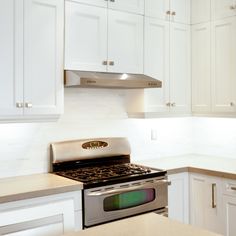 a kitchen with white cabinets and stainless steel stove top oven in the middle of it